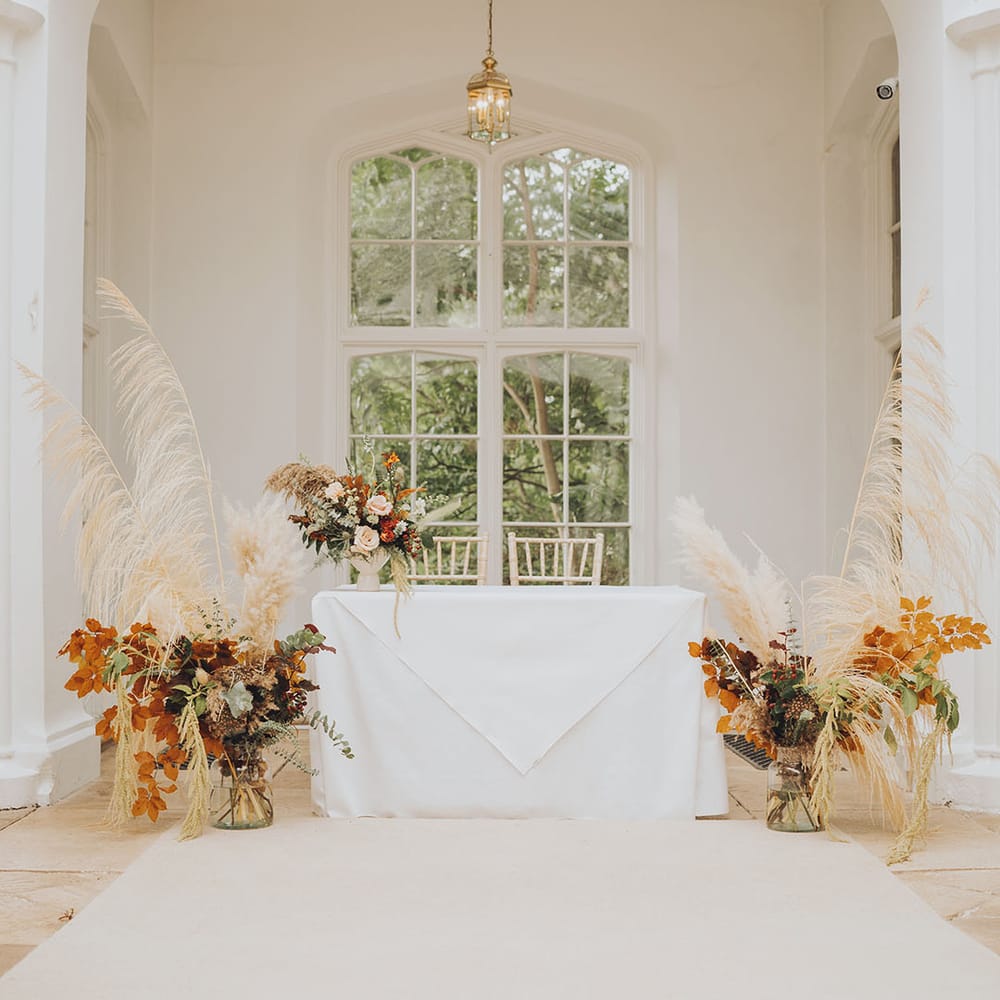 Pampas flower installations complete with dark foliage additions beside white table 