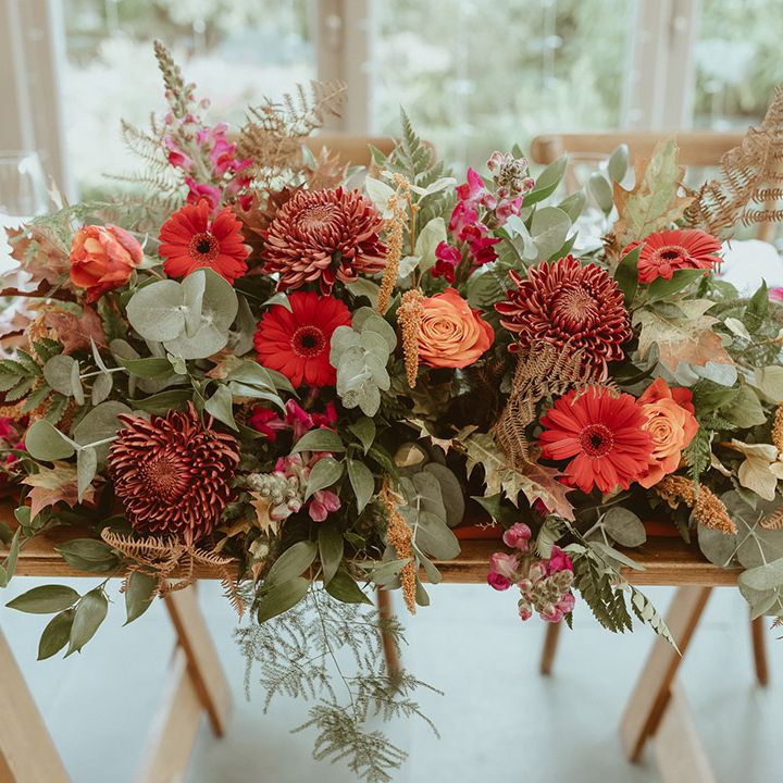 Autumnal wedding flower arrangement with red and orange flowers with roses, chrysanthemums, and foliage 