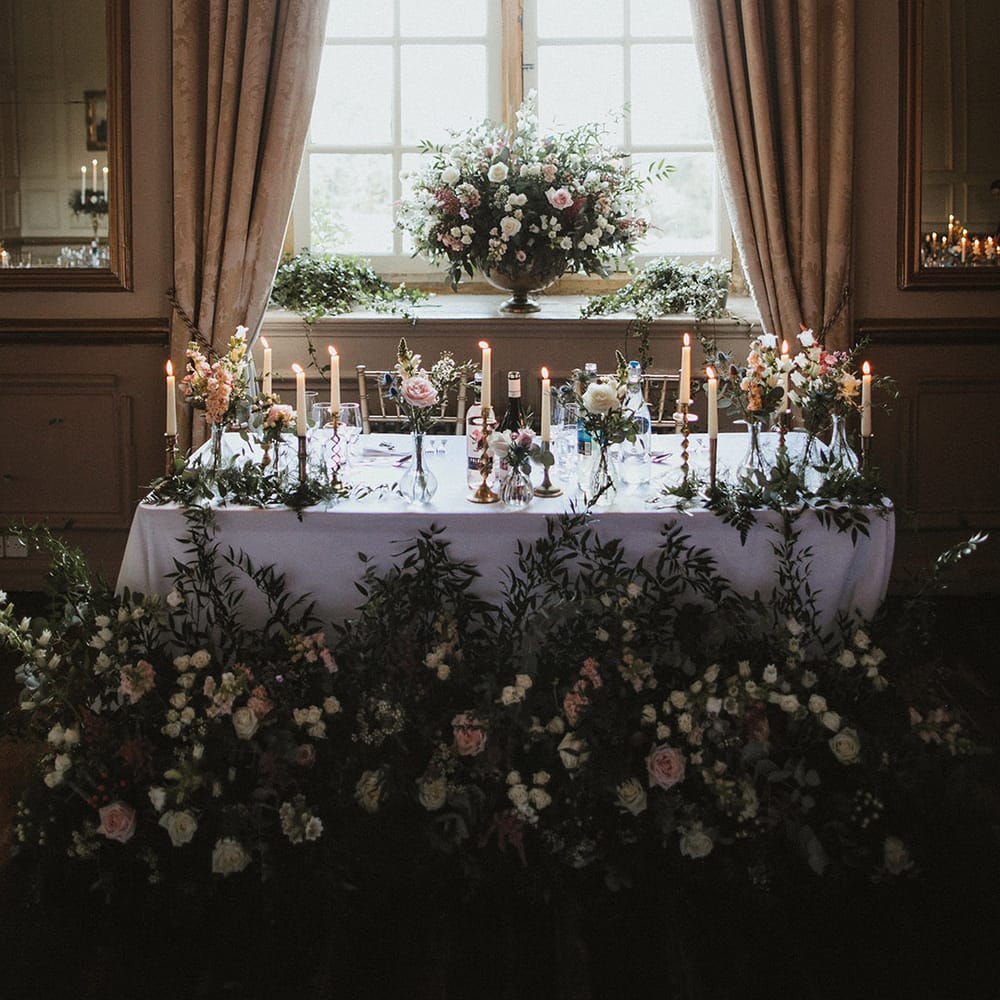 Pink and white rose wedding flower arrangements lining the top table and in vases on the window sill 