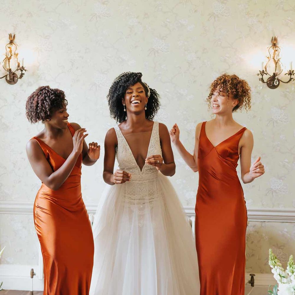 Bridesmaids in satin slip burnt orange bridesmaid dresses standing with bride in v neck princess wedding dress - hen party ideas 