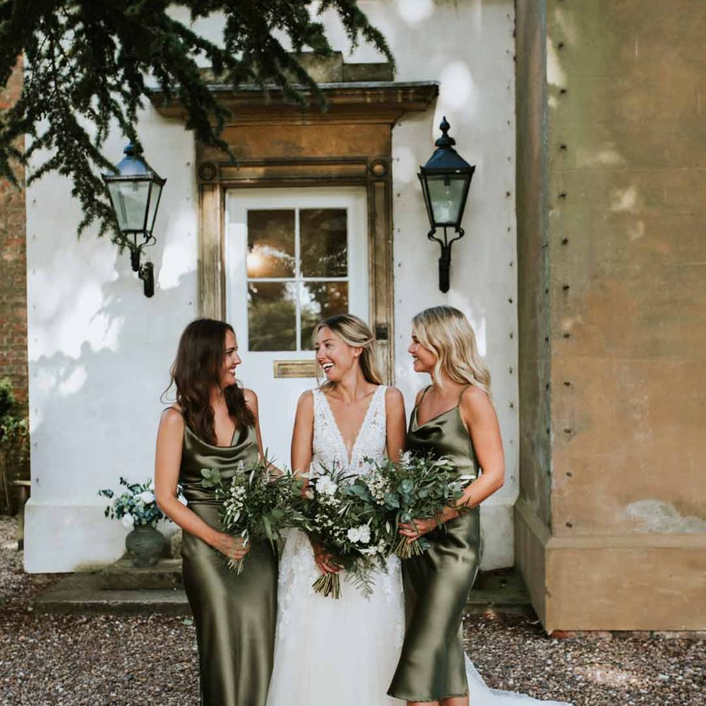 Bride in deep v neck princess wedding dress standing with bridesmaids in cowl neck sage green midi bridesmaid dresses 