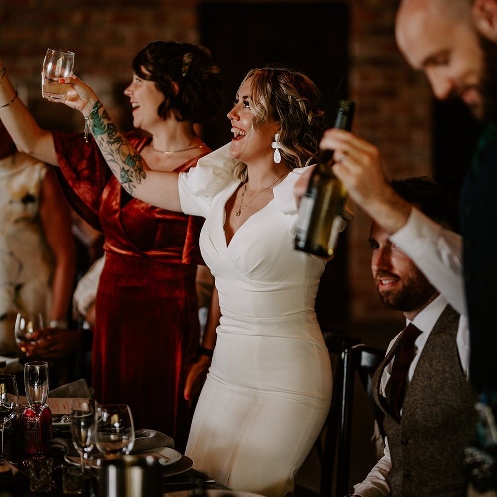The bride drinks at the wedding breakfast wearing a fitted wedding dress 
