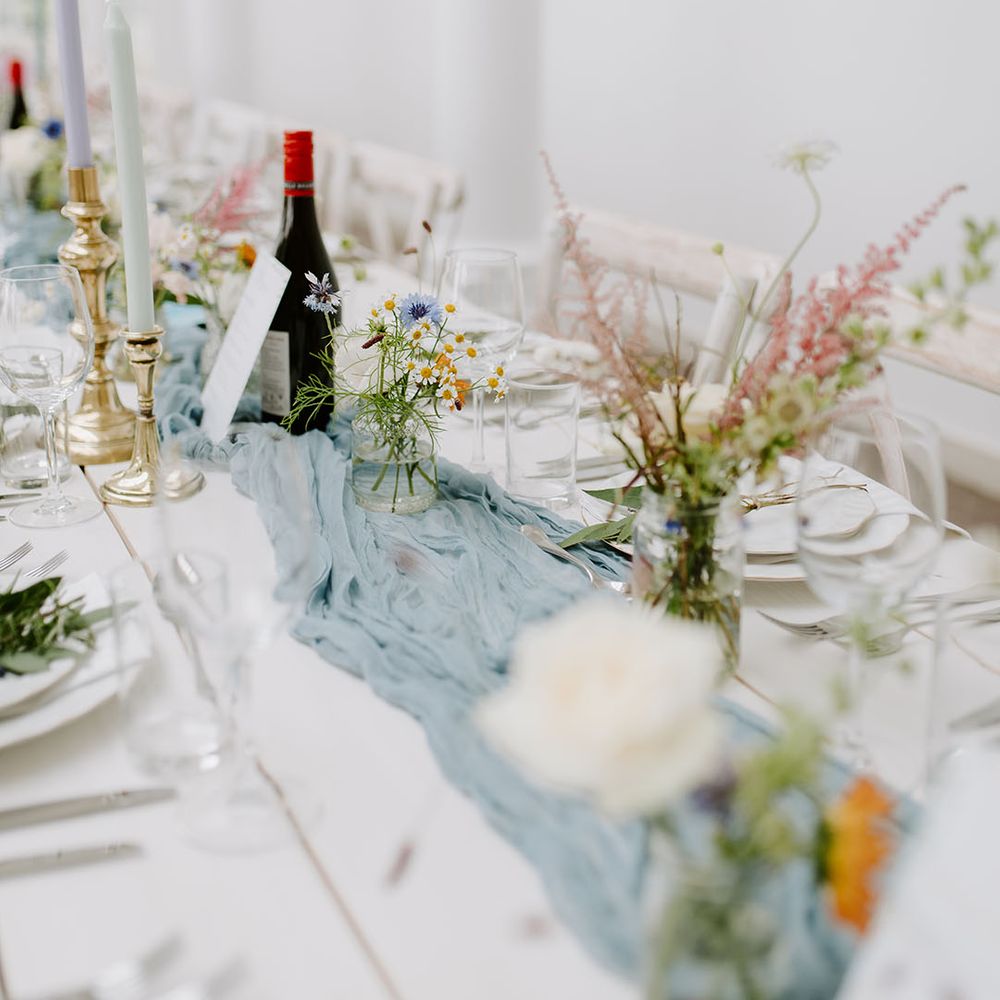Bud vases with pastel wedding flowers with dusty blue table runner on long banquet tables 