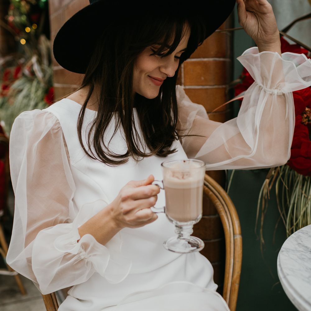 Bride in Knee length wedding dress and fedora hat enjoying a coffee at intimate wedding