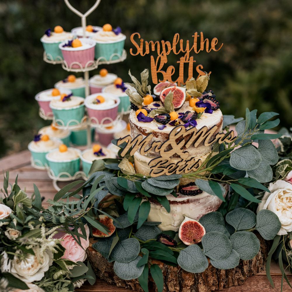 Wedding cake and cupcakes on wooden table with foliage decoration 