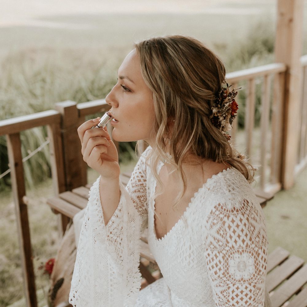 Bride applies lipstick in crochet wedding gown 