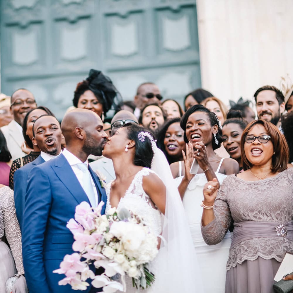 Bride and groom kissing surrounded by friends and family 