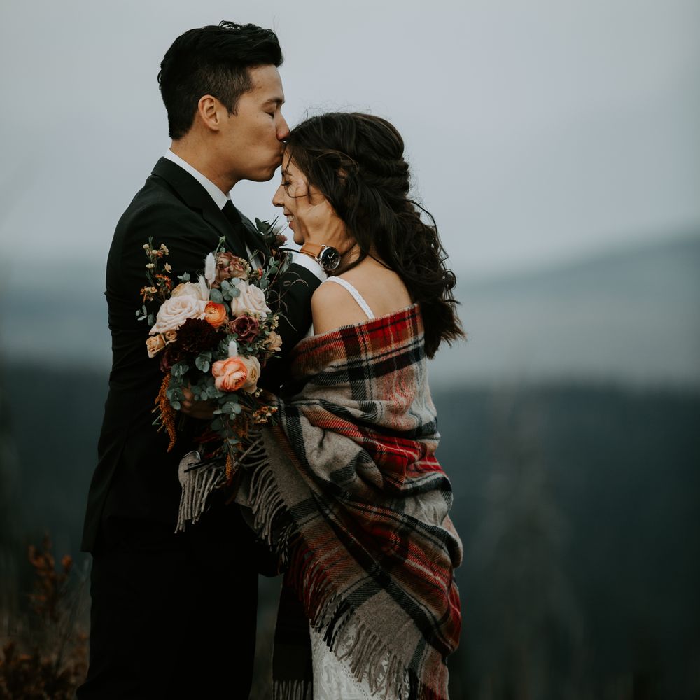 Groom kisses bride on the forehead with mountains in the background