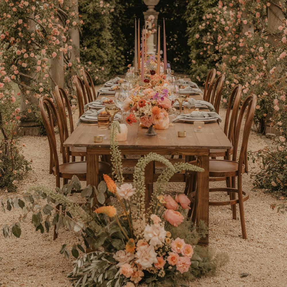 Outdoor wedding reception at Euridge Manor with tall coloured taper candles in gold candlesticks surrounded by pastel orange wedding flowers 