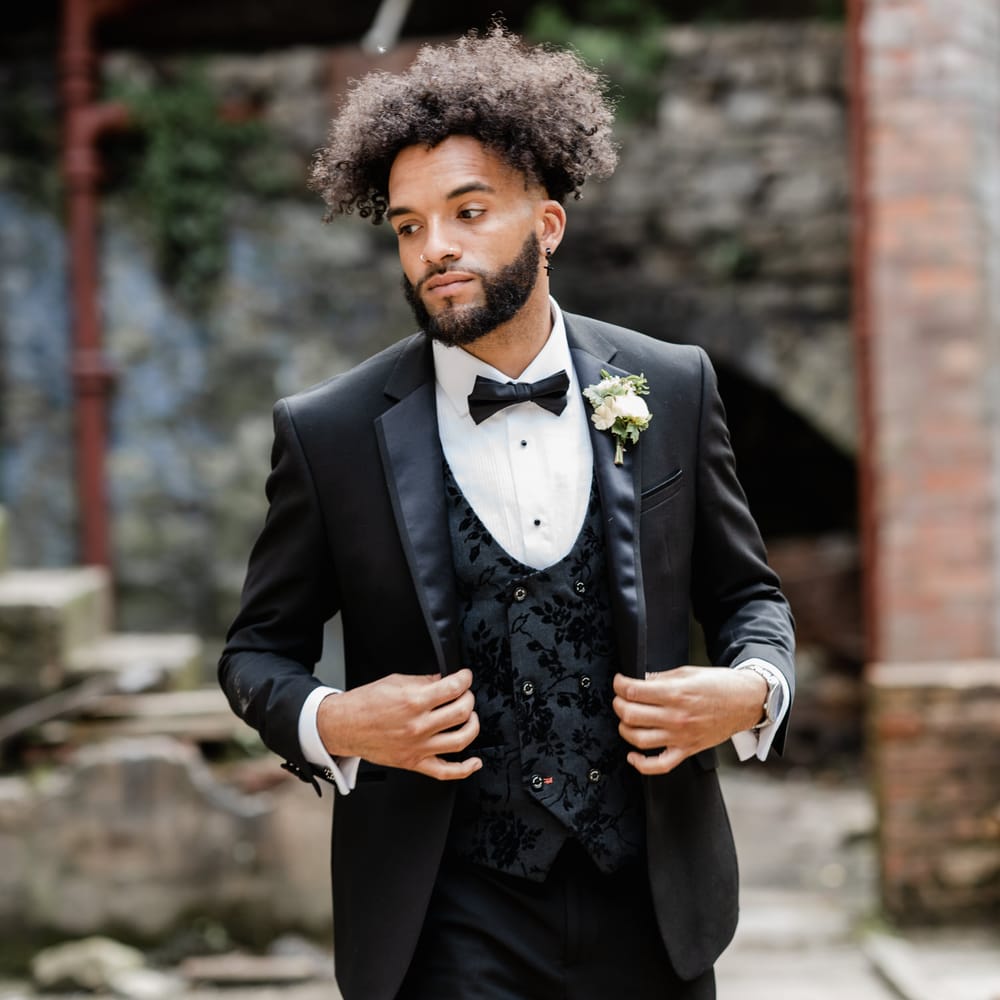 Stylish groom in a three piece black tuxedo with bow tie and jacquard, double breasted, horseshoe waistcoat 
