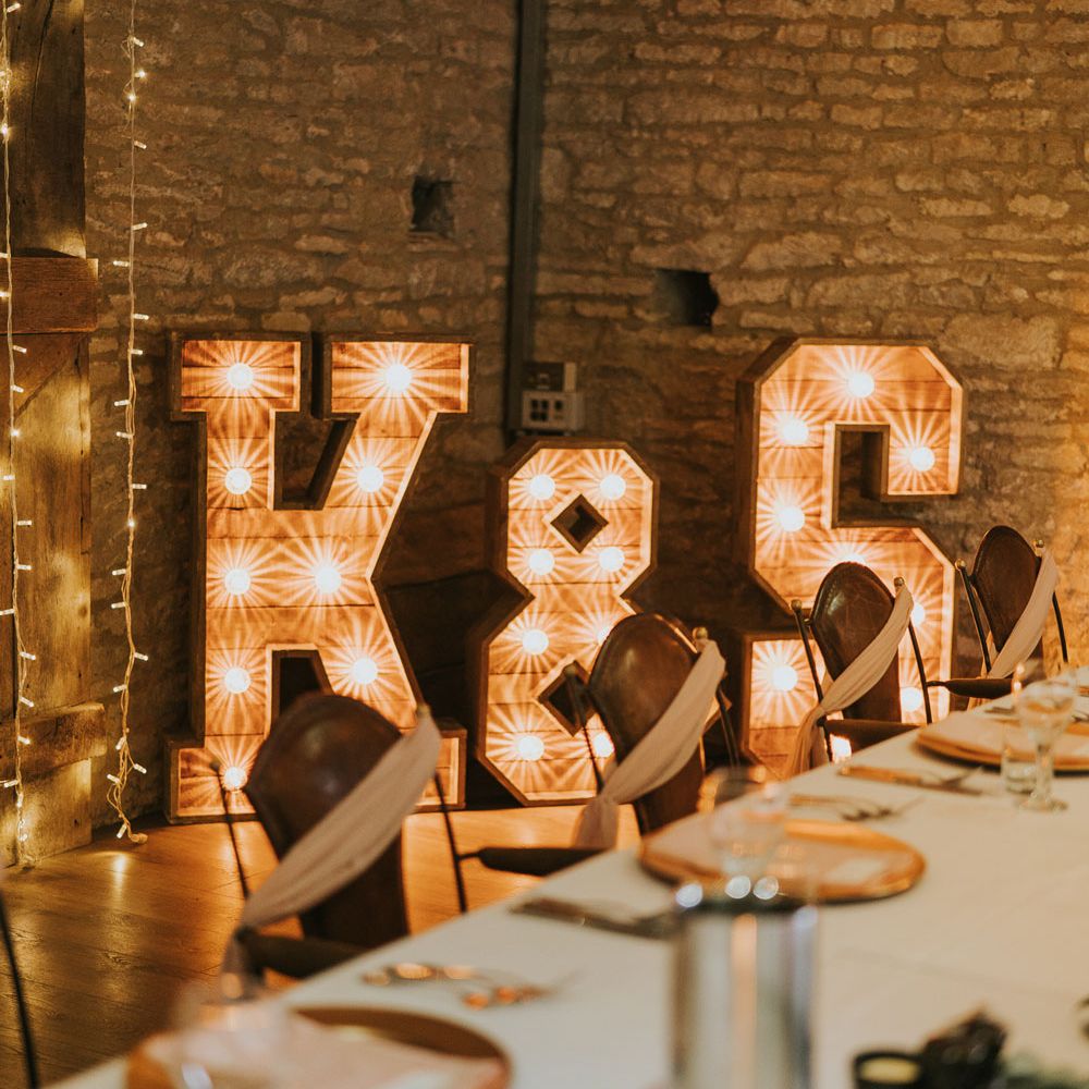 5ft bulb letter signs reading 'K & S' in stone room lit with fairy light strings at Tythe Barn wedding with barn wedding flowers