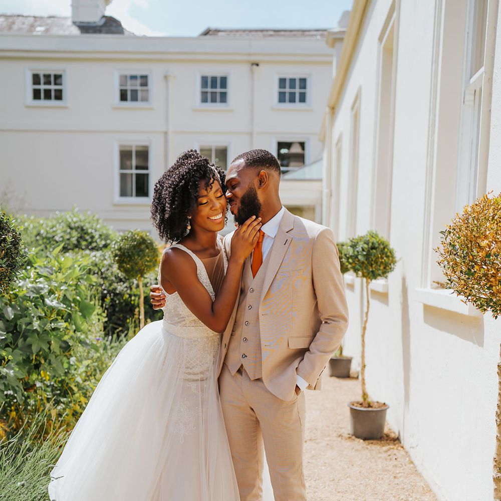 Groom in a beige three-piece suit kissing his bride in the courtyard at Modern Hall, London in a plunging neckline wedding dress by Ersa Atelier