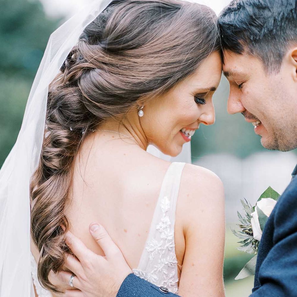 Groom in blue wool jacket touching his brides back with a low V and long curled hair 