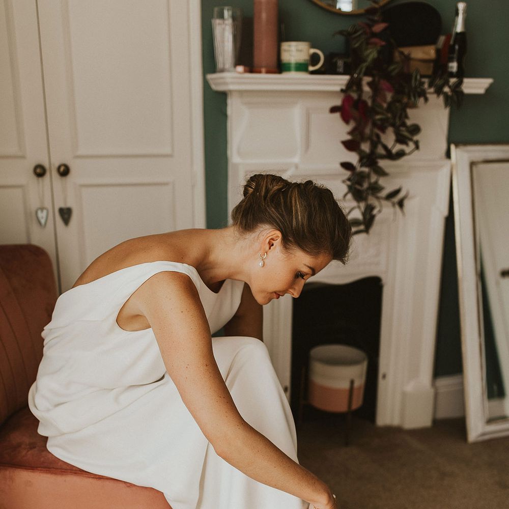 Bride in a Charlie Brear wedding dress putting on her Loeffler Randall plissé-organza sandals