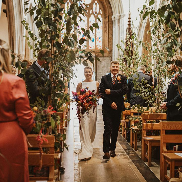 Father of the bride walking his daughter down the church aisle decorated with trees 