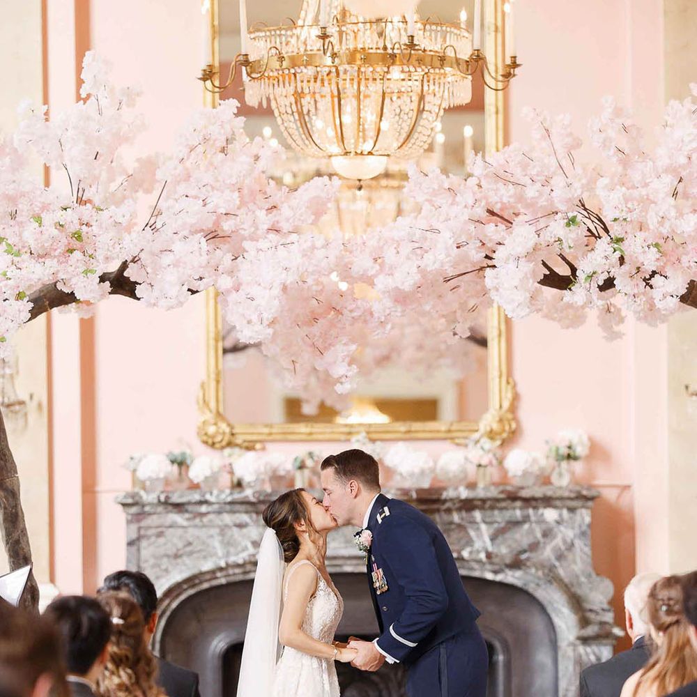 Bride & groom kiss under blossom archway on their wedding day during ceremony