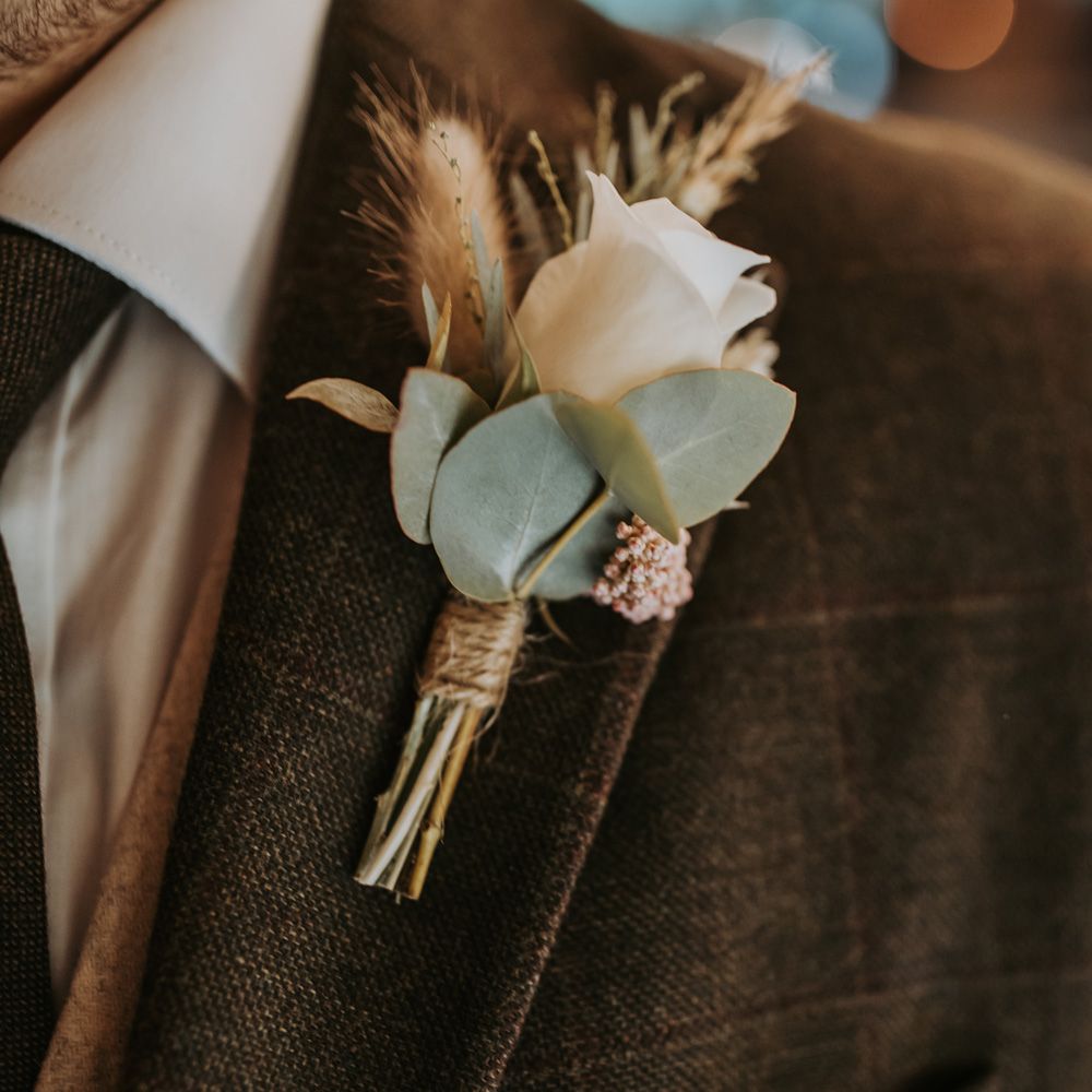 Groom in brown wedding suit with white rose buttonhole and dried floral details 