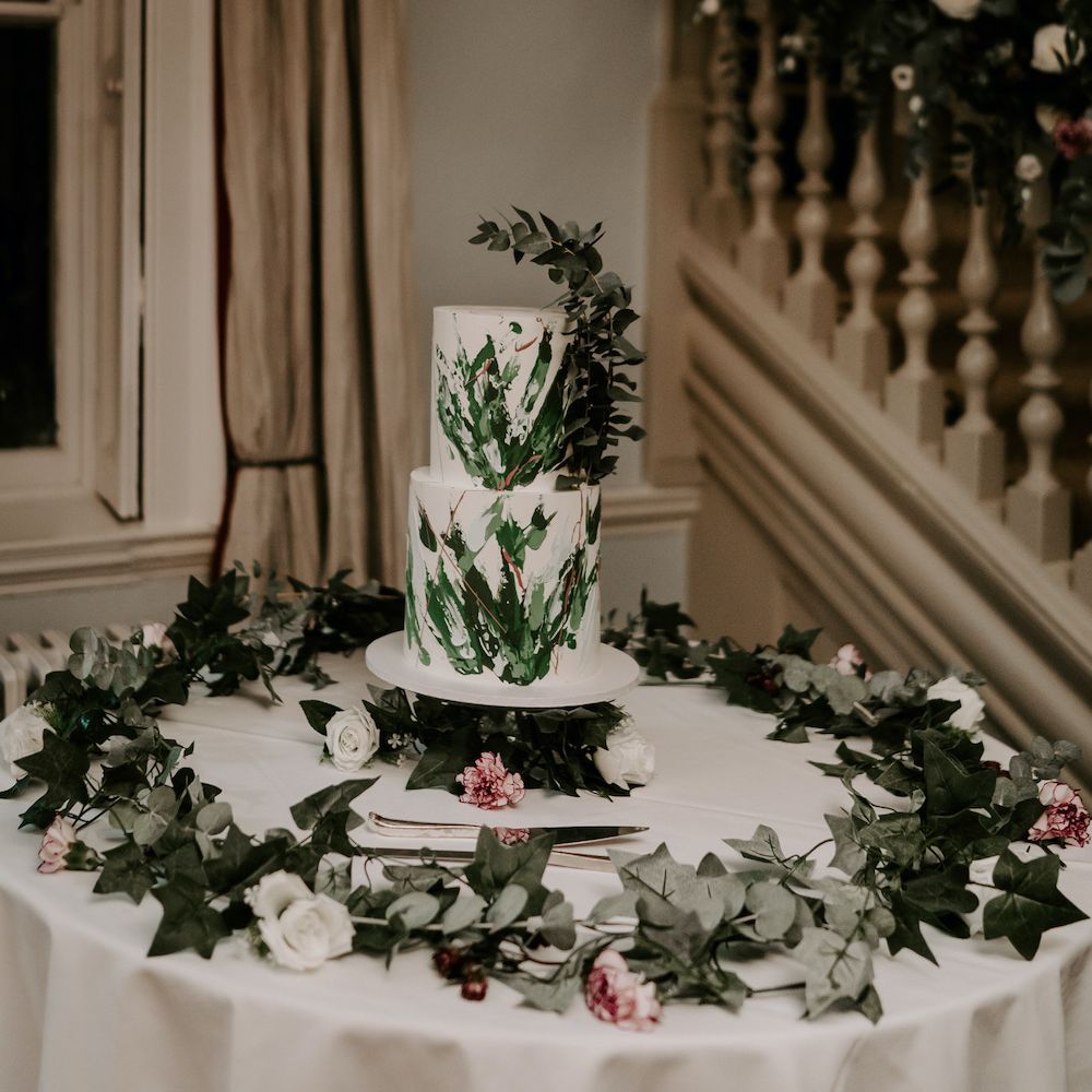 Two tier white wedding cake with sage green leaves and embellishments 
