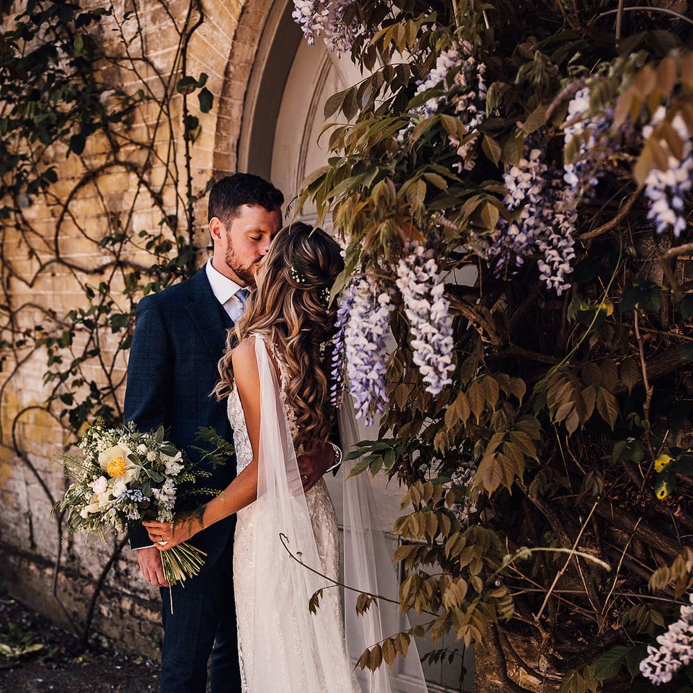 Bride in lace wedding dress with detachable tulle wings and groom in blue three piece suit kiss 