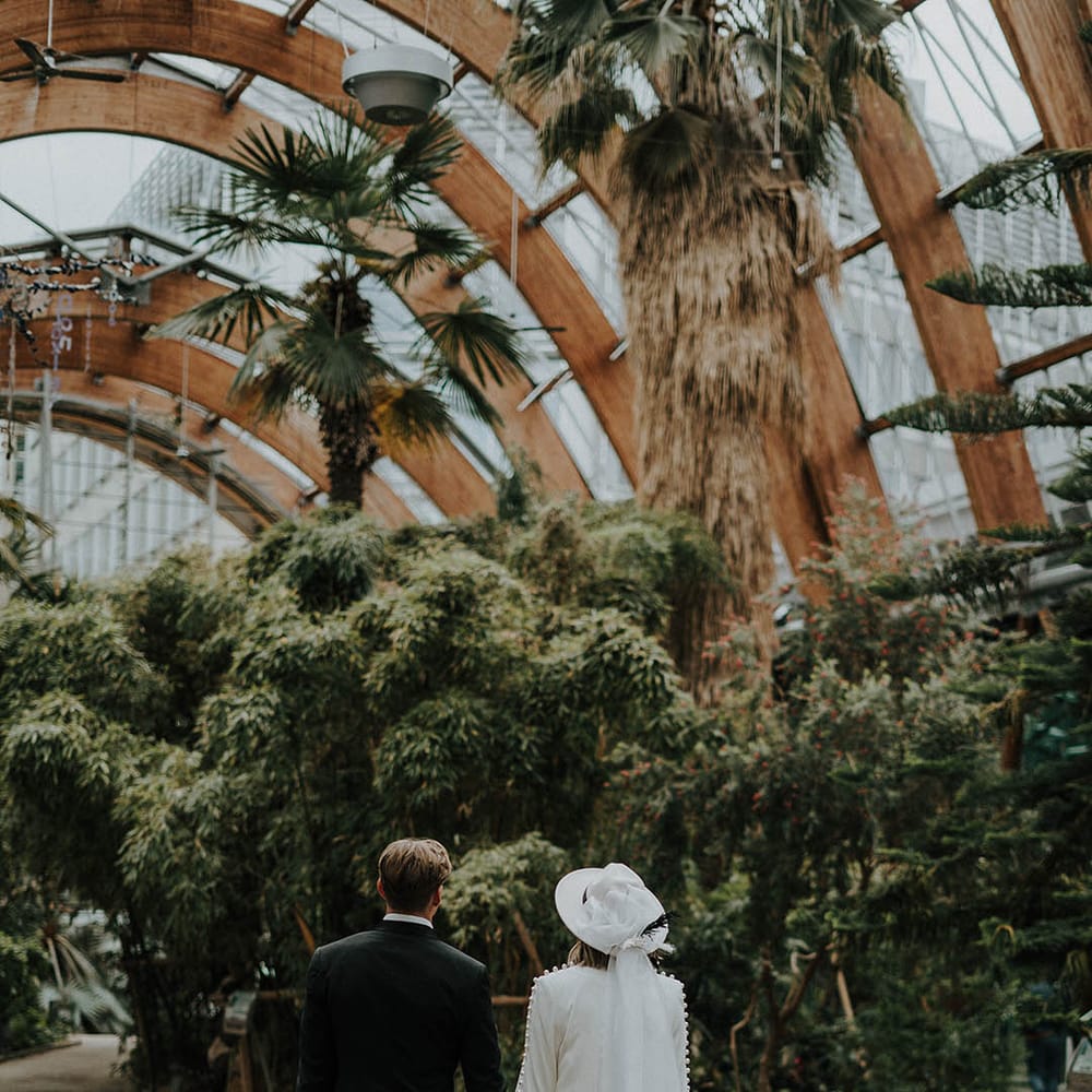 Bride in white wedding trouser suit holding hands and walking with groom in black tie