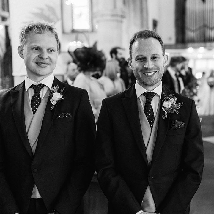 Groom smiles at the camera with his best man standing next to him in matching suits 
