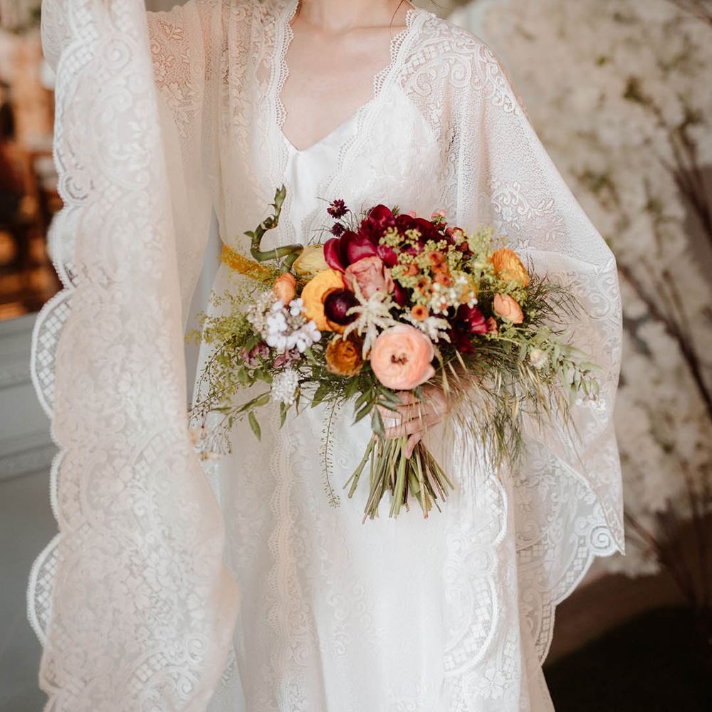 East Asian bride in a lace kimono style wedding dress with natural makeup holding a red, orange and yellow wedding bouquet at Japanese wedding 