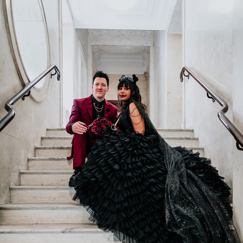 Bride's ruffled wedding dress drapes across staircase as she sits with her groom on their wedding day