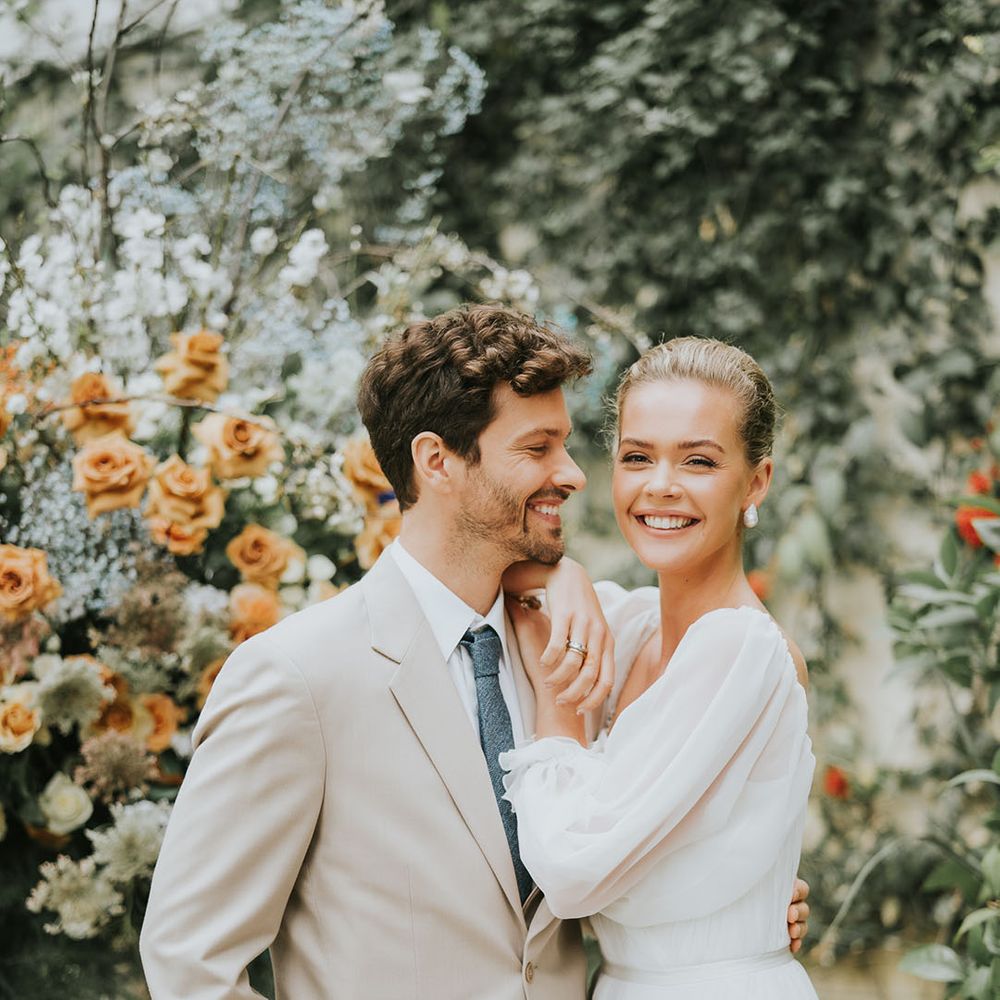 Groom smiling in a beige suit with blue tie embracing bride in a romantic wedding dress for wedding at Sezincote House 