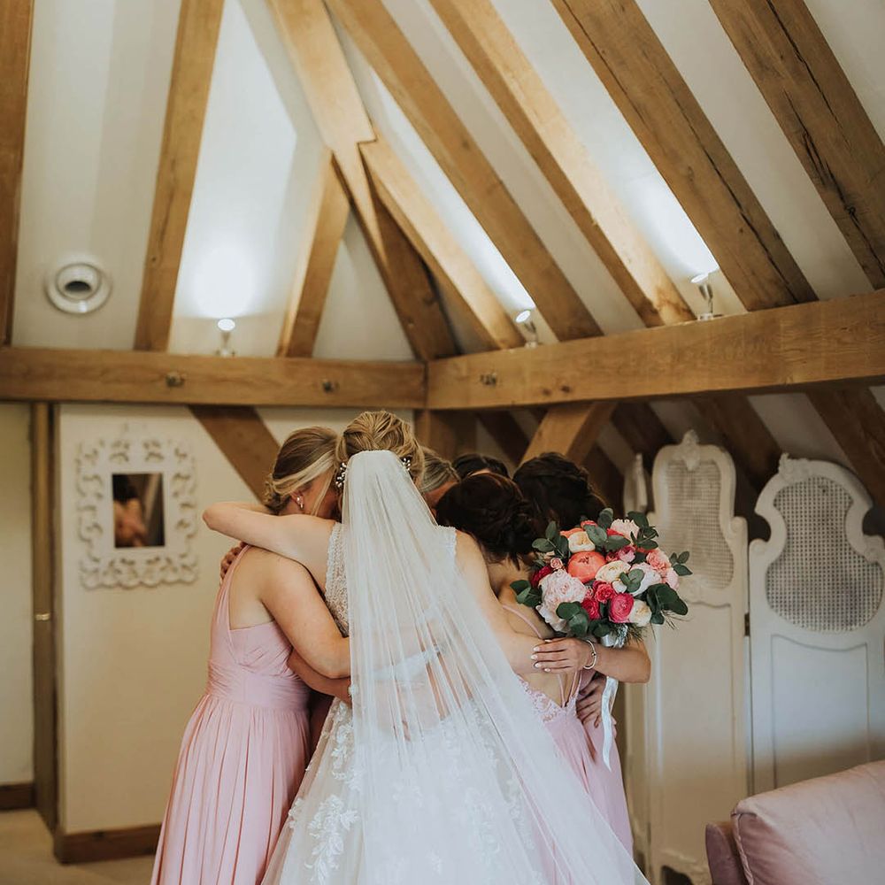 Bride in a floral lace wedding dress has a group hug with her bride tribe in pink dresses before the wedding 