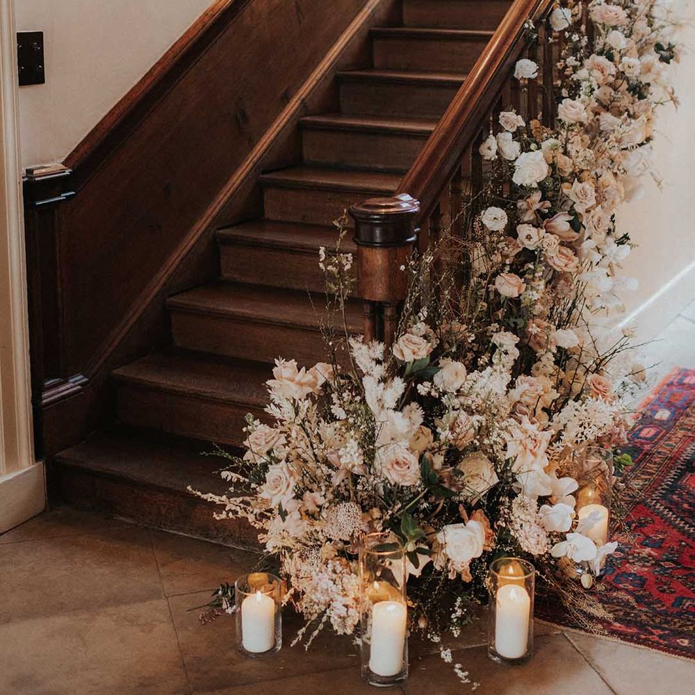 Three pillar candles in glass display cases with pink and white rose floral arrangements on staircase at Iscoyd Park