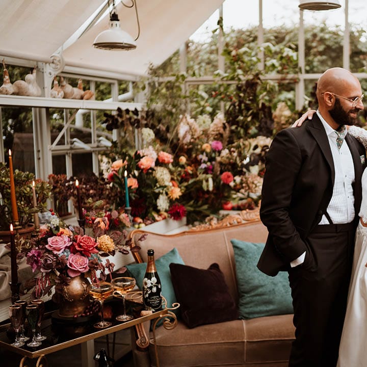 Bride in three quarter length sleeve bridal separates with lace detailing and full satin skirt embracing groom in black tuxedo with hand painted silk cravat and handkerchief 