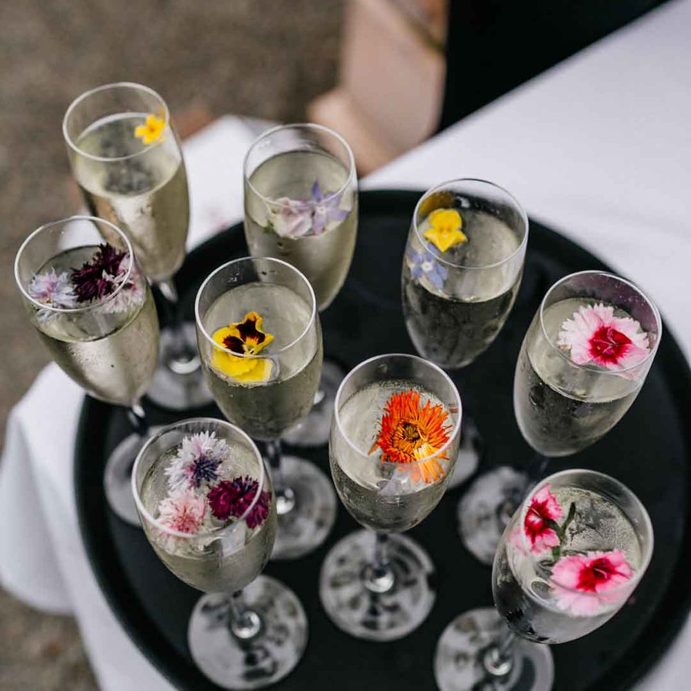 Black tray containing champagne flutes with champagne and edible flowers 