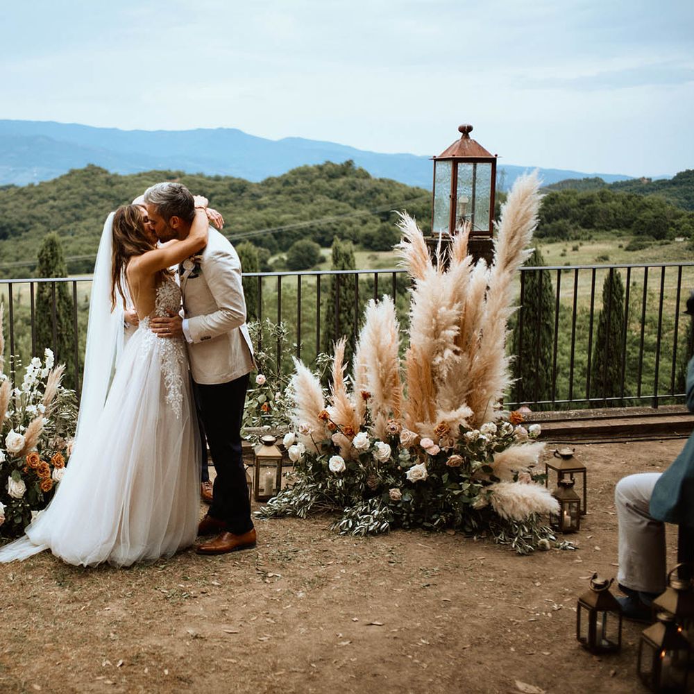 Bride and groom kiss at altar surrounded by pampas grass and rose decor in the Tuscan hills at destination wedding ceremony