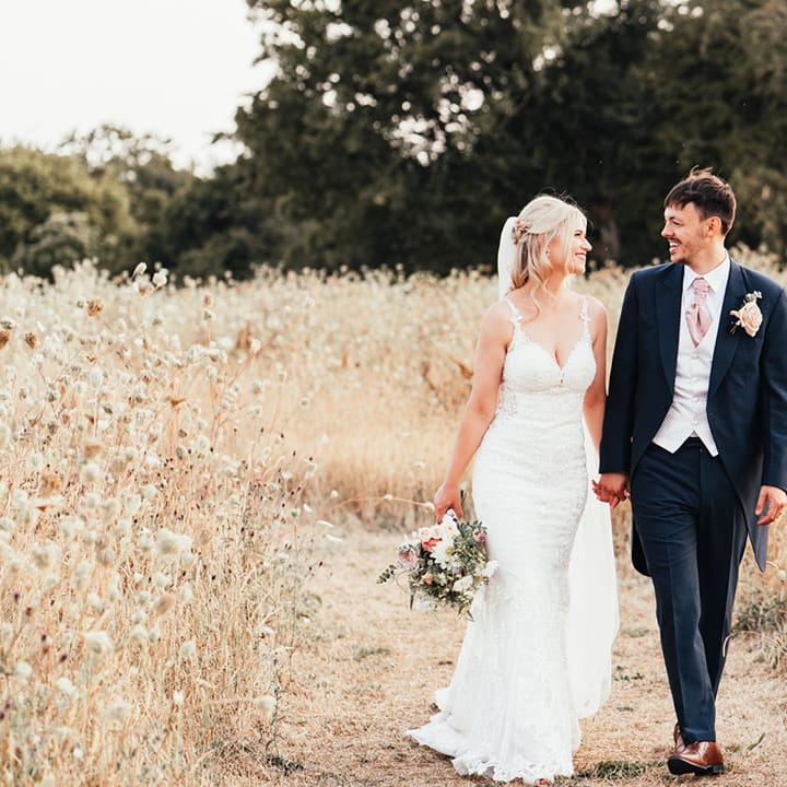 Bride walking along the grounds at Rackley Chiltern Hills barn wedding venue hand in hand with the groom in a navy suit 