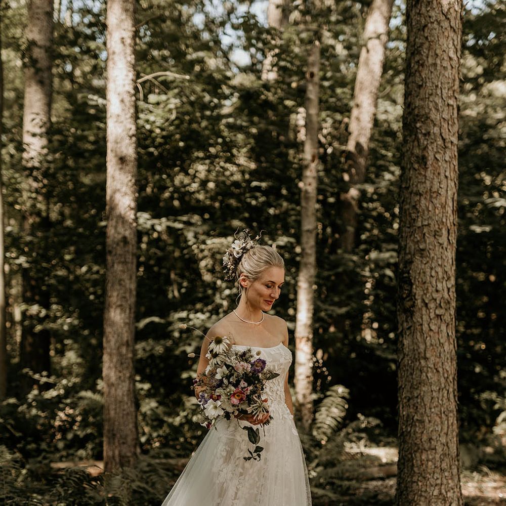 Bride in floral strapless wedding dress for woodland wedding with her hair in a chic updo decorated with purple and white wedding flowers 