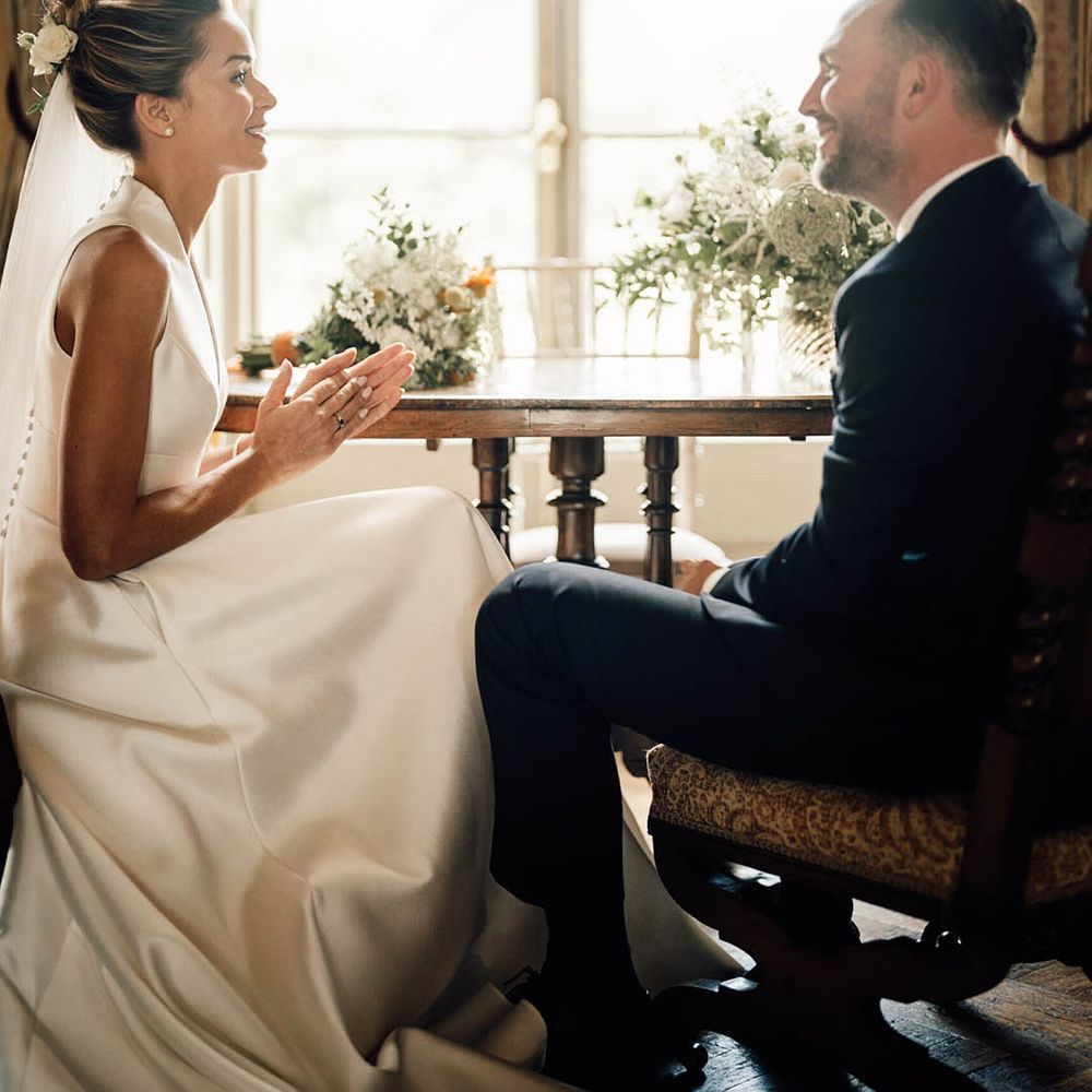 Bride in classic Sheila Harding wedding dress sitting with groom for their country house wedding 