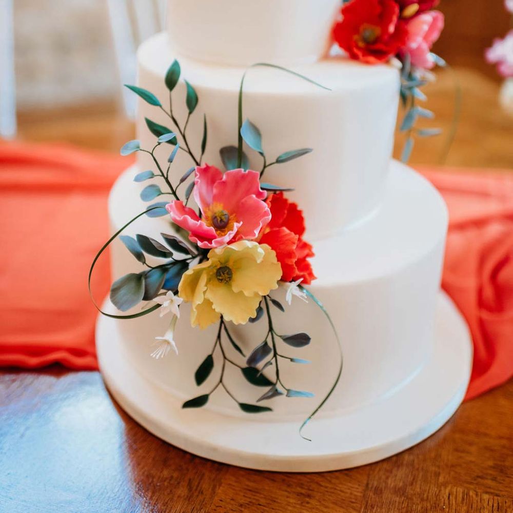 Misshapen three tiered wedding cake with white icing and seasonal flower and foliage cake toppers 