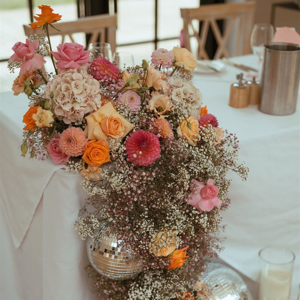 Pink and orange wedding flower decorations with gypsophila, roses, dahlias and more with disco balls 