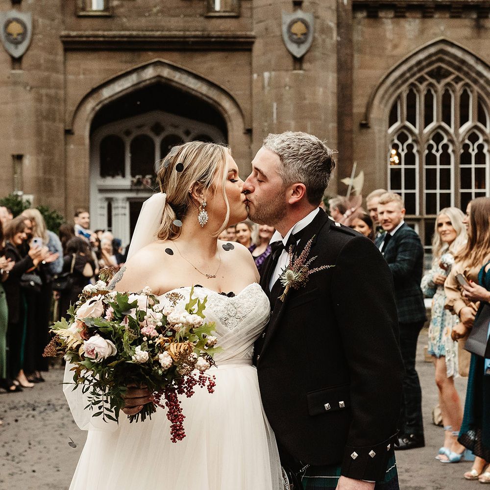 Scottish wedding with the bride and groom sharing a kiss as they are covered in black confetti 