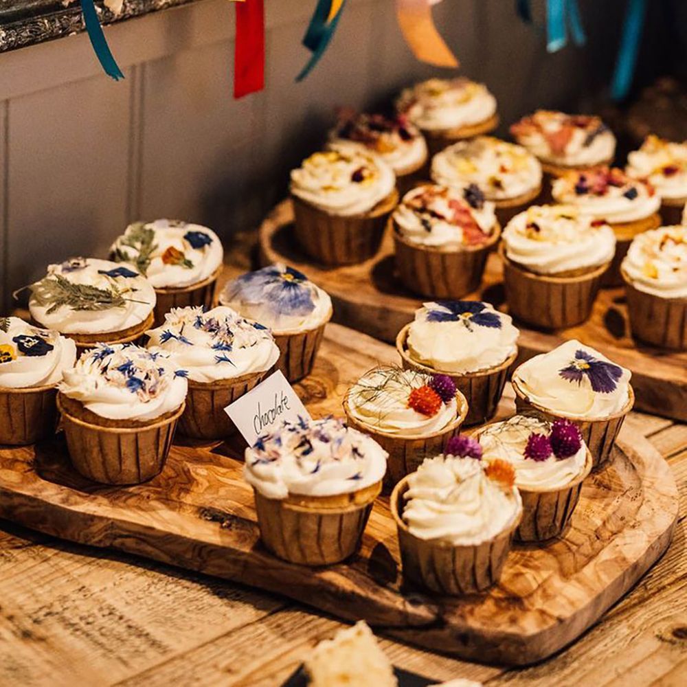 Tray of flavoured cupcakes with white frosting decorated with edible flowers 