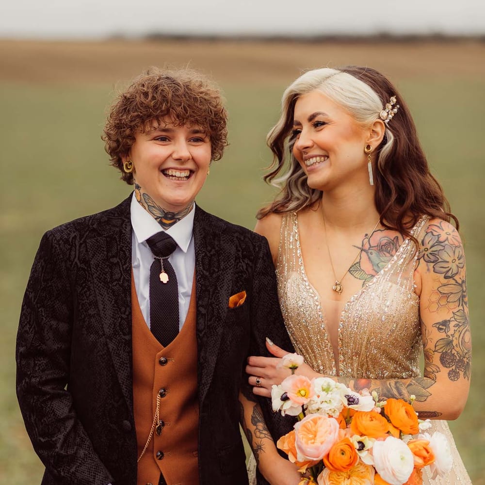 LGBQTIA+ wedding inspiration with bride wearing a gold wedding dress with orange and yellow wedding bouquet and bride in snake skin suit jacket 