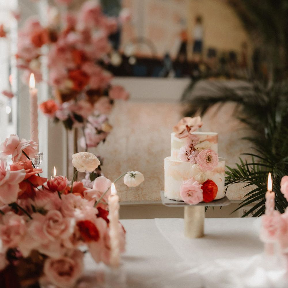 Two tier white wedding cake with brush effect detail, surrounded by pink wedding flowers and pink tapered candles