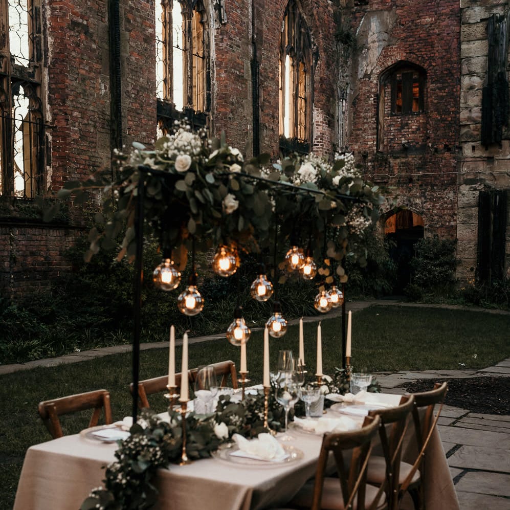 Outdoor wedding reception with festoon light installation and foliage table runner 