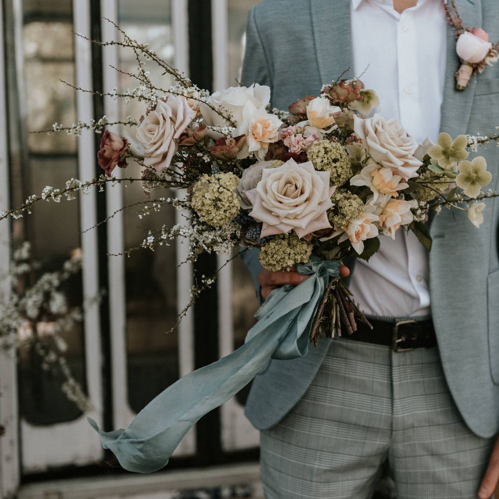 Grooms wears pale blue suit with tartan trousers whilst carrying floral bouquet 