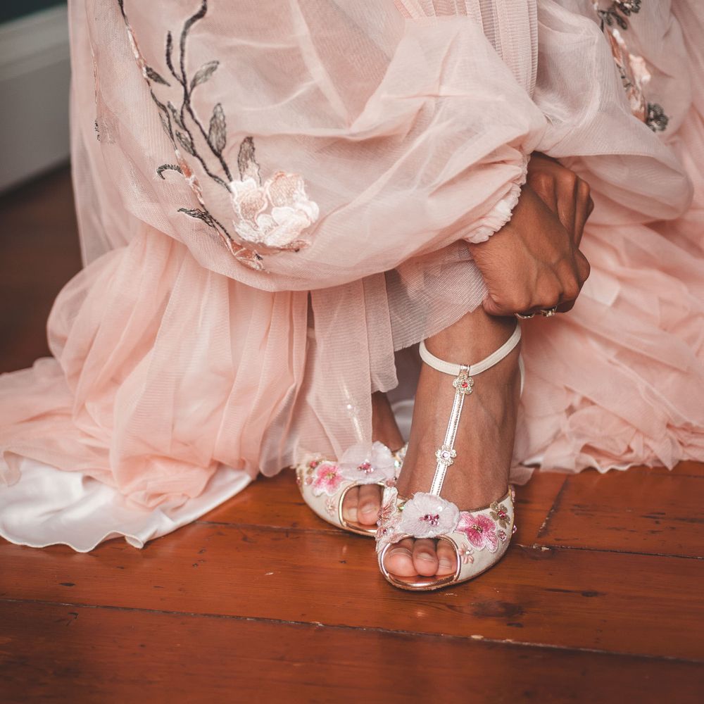 Bride in a blush pink dress leaning down to put on her peep toe T bar wedding shoes 