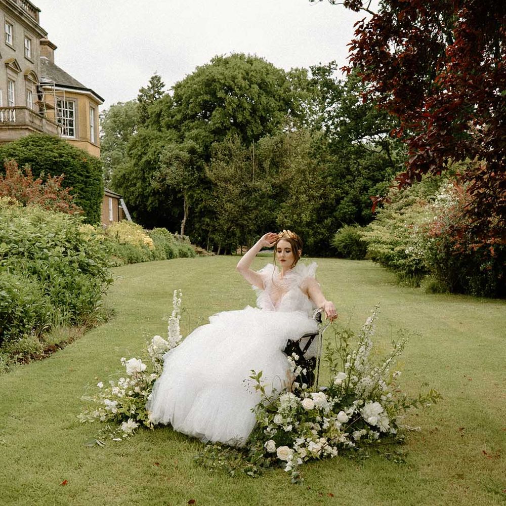 Beautiful bride in a wheelchair sitting in the gardens at Bourton Hall surrounded by white and green floral arrangements 