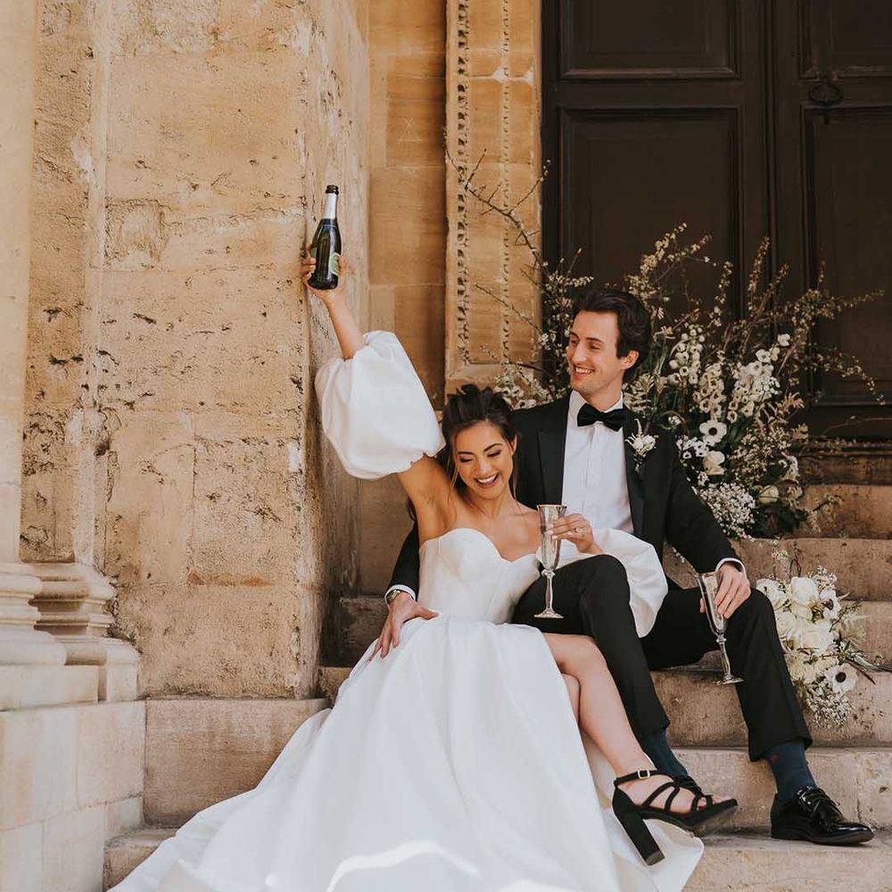 Bride and groom sipping champagne on the steps at Bodleian Library in a tuxedo and Nortier Shallow wedding dress