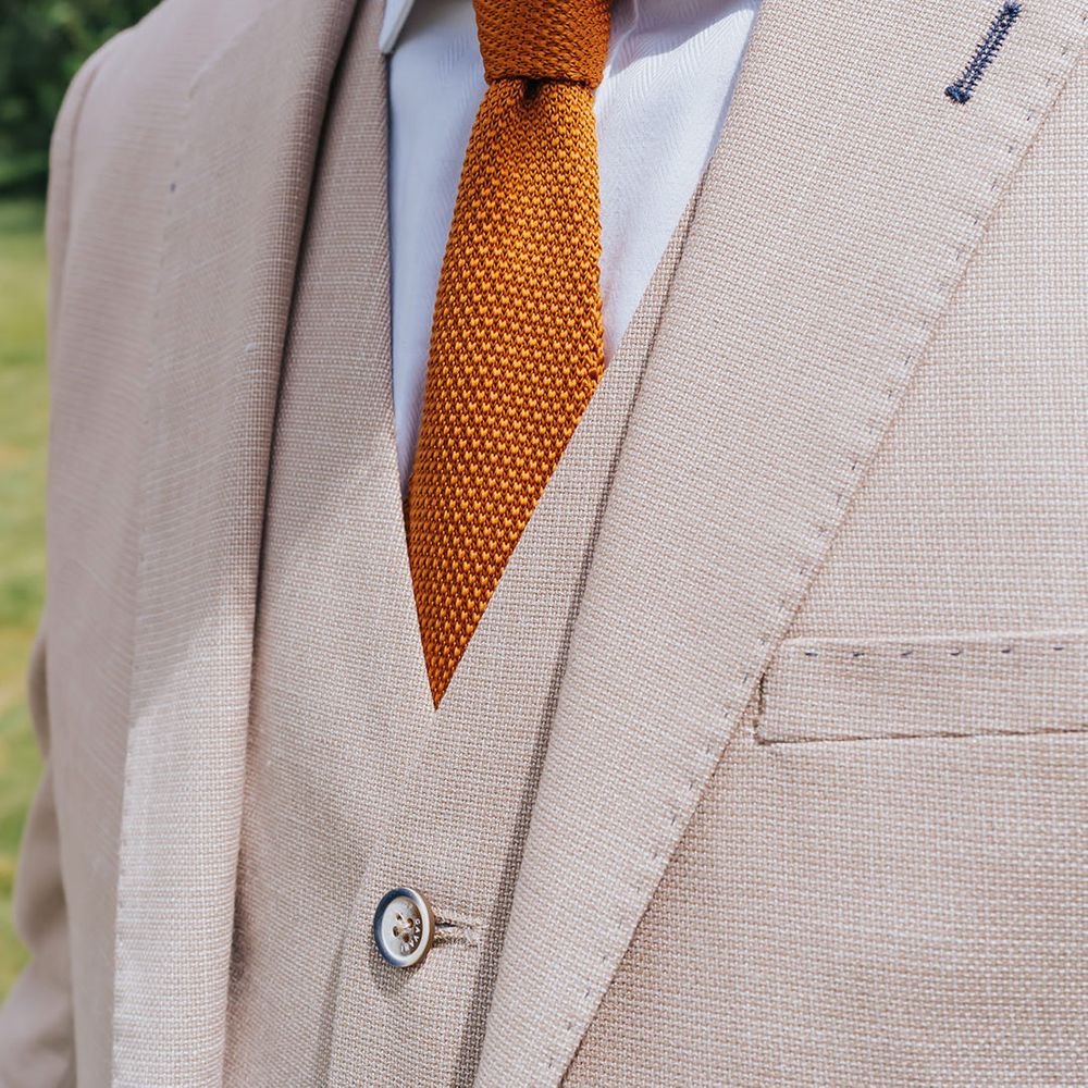 Groom in a beige three-piece suit with white shirt and orange waffle tie