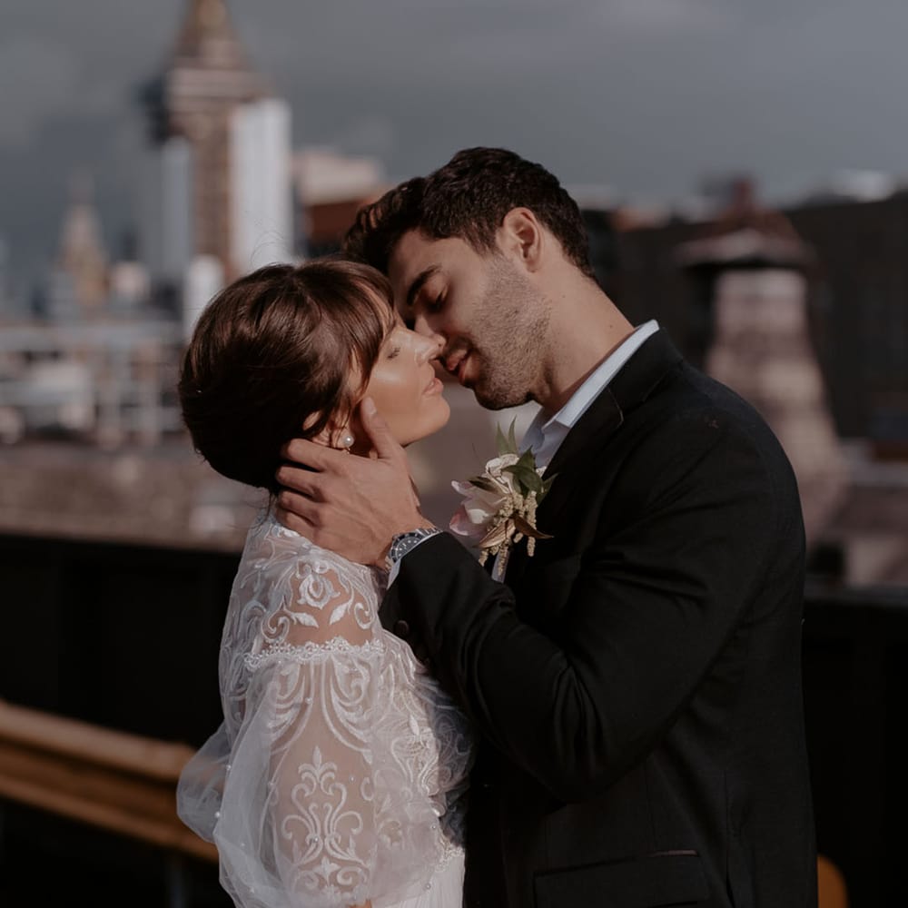 Groom in a black suit kissing his bride in a lace and tulle wedding dress with short puff sleeves and chic bridal up do 