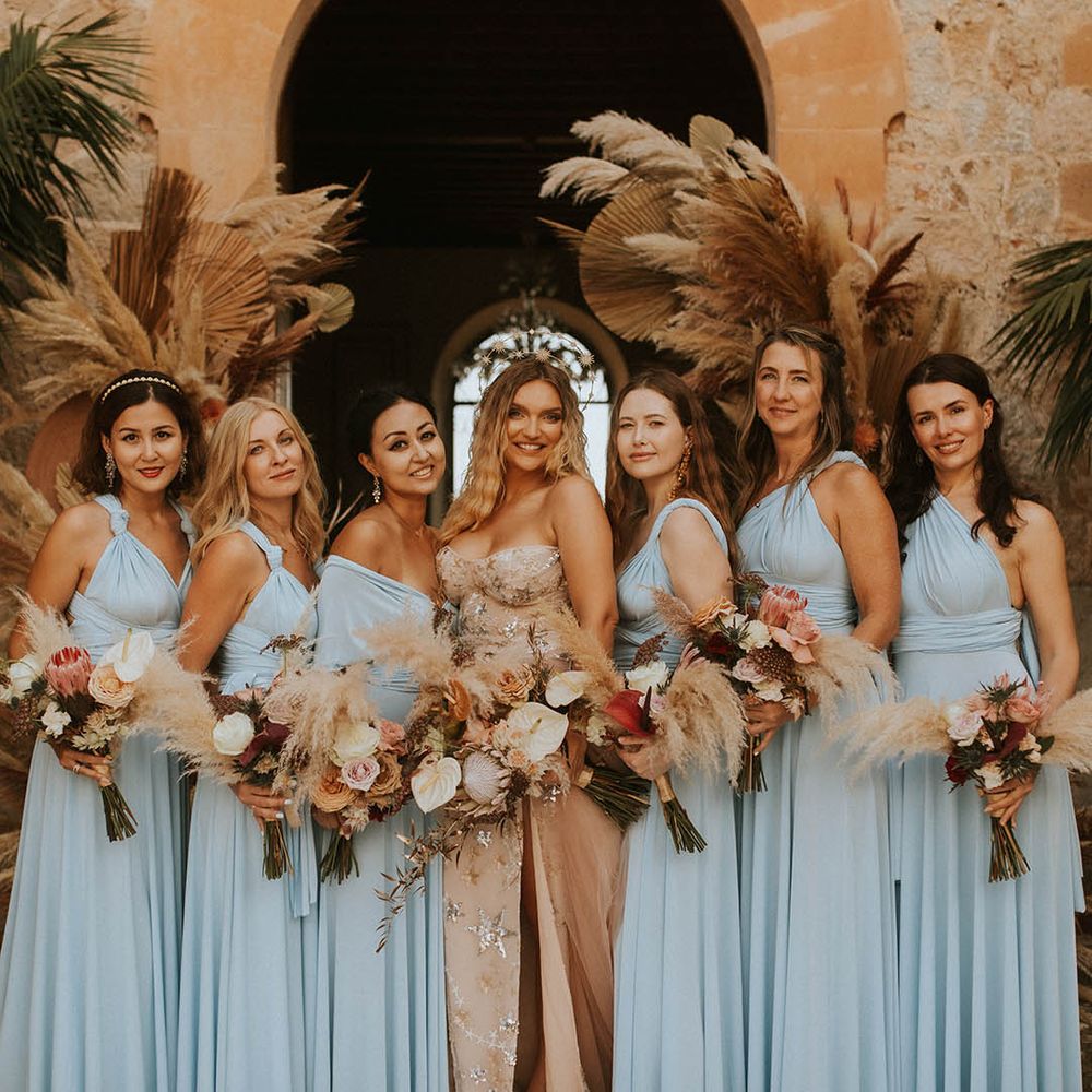 Bride stands with her bridesmaids who wear dusty blue gowns
